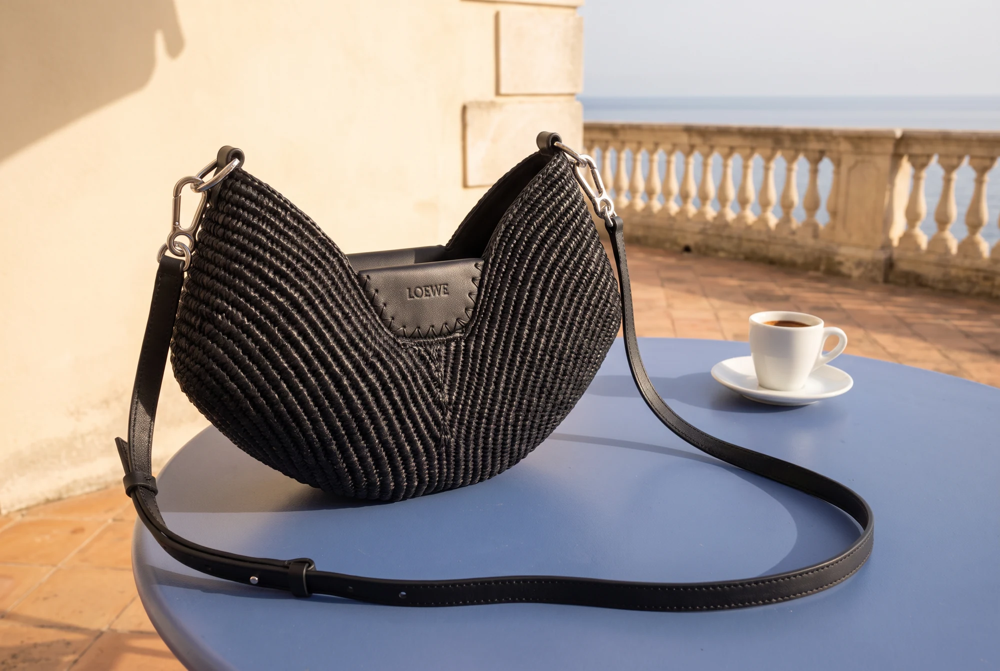 Detalle del bolso negro Loewe sobre una mesa azul junto a una taza de café