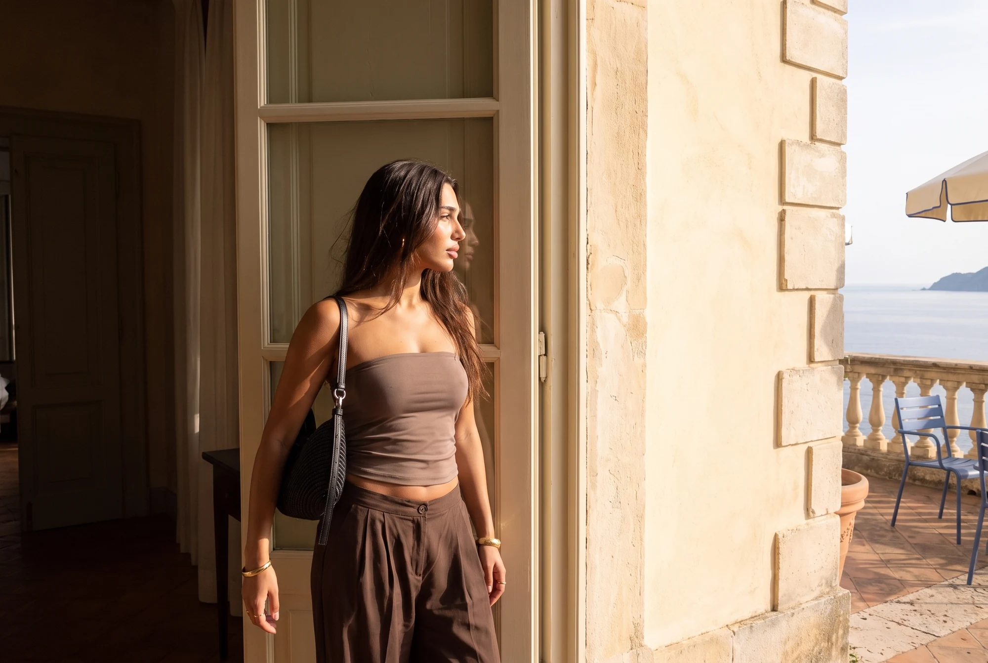 Modelo con conjunto marrón y bolso negro Loewe junto a una puerta de la terraza